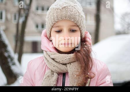 Sad child girl in warm knitted winter clothes spent time outdoors and got frozen. Stock Photo
