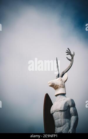 Vertical shot of a concrete statue of a deer surfer in Nazare, Portugal under a rainy cloudscape Stock Photo