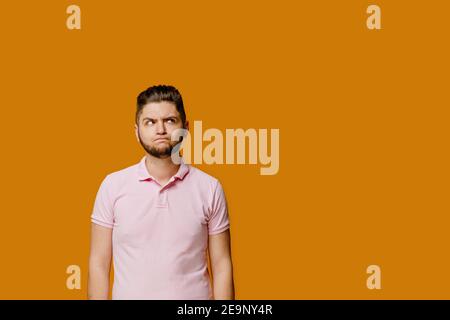 Young handsome man stands over orange background and smiles. Confident man wears pink shirt and looks in camera. Bearded caucasian business man. Stock Photo