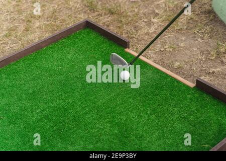 Playing in mini-golf on the green grass using niblick. Player hits white ball. Golf sport game. Advert for golf club Stock Photo