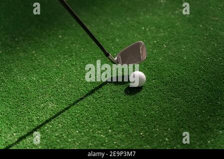 Playing in mini-golf on the green grass using niblick. Player hits white ball. Golf sport game. Advert for golf club Stock Photo