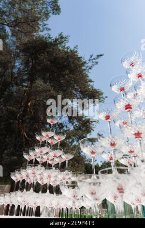 Pyramid of glasses with champagne and red cherry inside on business meeting at summer day. Alcohol cocktails for guests. Business meeting open air wit Stock Photo
