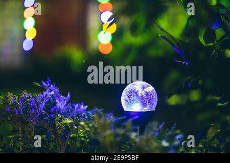 Night View Of Flowerbed Illuminated By Energy-Saving Solar Powered Colorful Multi-colored Lantern On Yard. Beautiful Small Garden With Blue Light Stock Photo