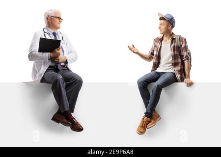 Full length shot of a mature doctor and a teenage male student sitting on a blank panel isolated on white background Stock Photo