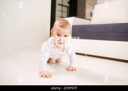 Baby boy crawling at home in living room. Wearing white body