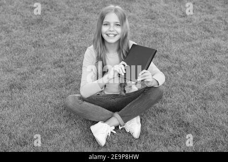 Girl reading book outdoors green lawn background, books shop concept. Stock Photo
