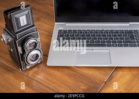 a modern laptop computer next to an antique twin lens camera, contrasting between modern and retro style Stock Photo