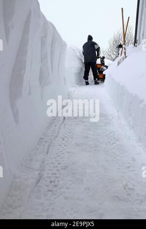 A man clears the sidewalk with a snow blower during heavy snowfall Stock Photo