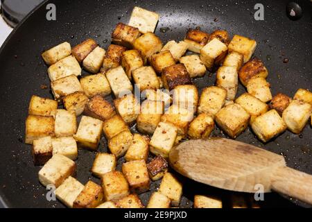 Marinated cubes of tofu being sauteed to golden colour in a stick free pan Stock Photo