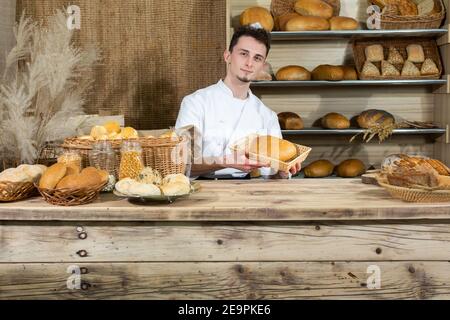 A clerk sits behind the counter serving his own baked goods. A handsome baker serves his customers in a family bakery store. Stock Photo
