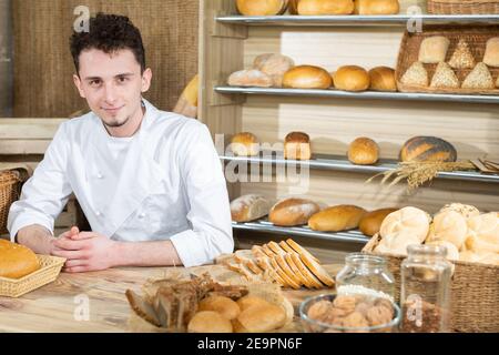A clerk sits behind the counter serving his own baked goods. A handsome baker serves his customers in a family bakery store. Stock Photo