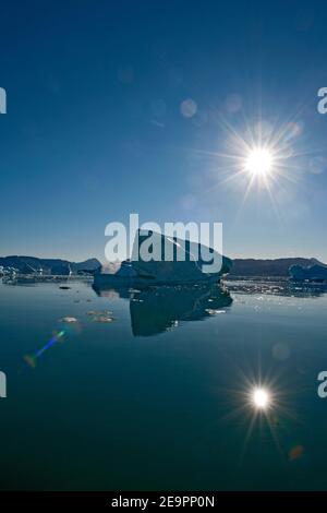 iceberg and sun reflecting in still fjord in South Greenland Stock Photo