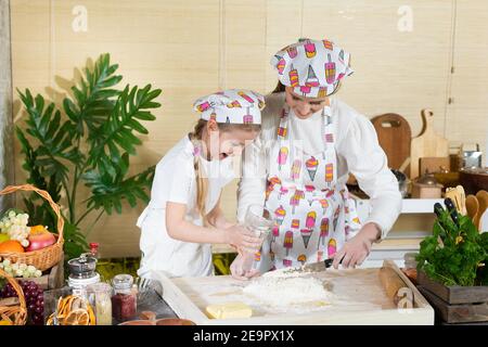From the glass of the girl, that is, mother and daughter, pour warm water into the wheat flour to make the dough in good proportions. . The joy of mom and daughter's moments together while working in the kitchen. Stock Photo