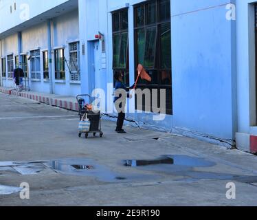 Bangkok, Thailand - February 2, 2021 : Blurred motion of female worker wearing face mask using mop with cloth to wipe glass window outside a building Stock Photo