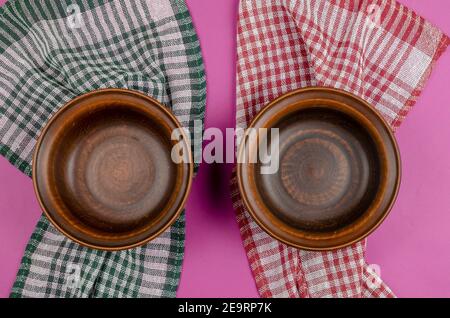 Empty bowls of red clay on a pink background. A Red and green checkered napkin lies under the bowl.  Top view, Flat Lay Stock Photo
