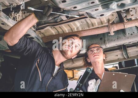 Man and woman auto mechanic working team checking under car for auto maintenance and service in garage Stock Photo