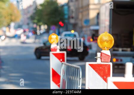 warning poles with orange light signal on the road about repairs work, blurred street with cars on background Stock Photo