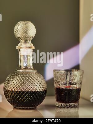 Jug of red wine and glass of wine, with unusual lighting in the form of patterns on the wall. Stock Photo