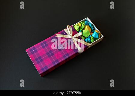 Colored gift box with satin bow with origami paper stars on black background. Gifts for the holidays Stock Photo
