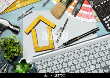 Small wooden house made of yellow toy blocks on the desk, with work tools, computer keyboard, calculator and Euro coins. Home improvement concept. Stock Photo