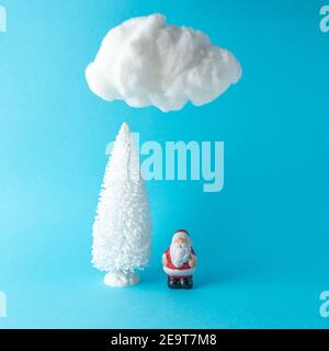 Snowy Christmas tree with small Santa Claus under cotton cloud on pastel blue background. Christmas or New Year minimal concept. Stock Photo