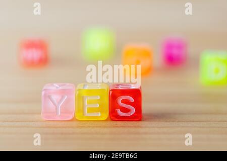 YES text with color letters cubes on wooden background. Minimal concept. Stock Photo