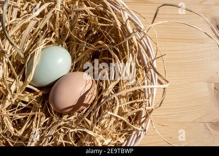 Organic Easter concept: Top view on a basket filled with straw and two natural colored eggs from the farm. Sun light falling on still life. Wood table Stock Photo