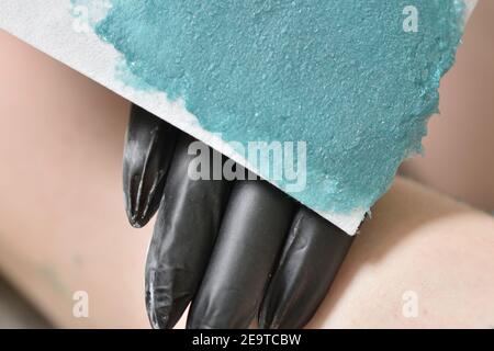 The process of female waxing. Beautician removes wax with hair from female legs. Stock Photo