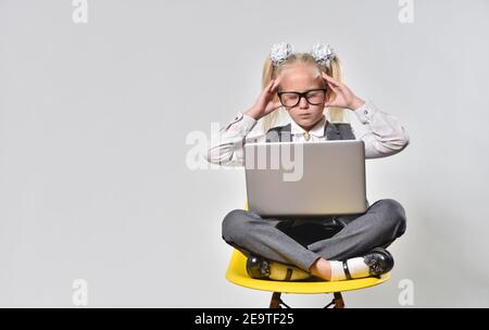 Girl child experiences stress while working at a laptop on a gray background Stock Photo