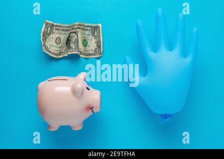 Piggy bank with a medical glove and crumpled dollar bancnote. Minimal Coronavirus outbreak. Saving money concept. Stock Photo