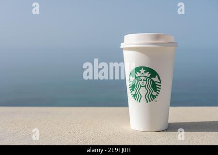 Heraklion, Greece - May 16 2020: White cup of coffee with Starbucks logo on sea background. Stock Photo