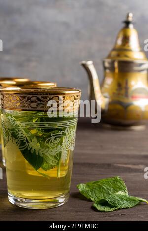 Close-up of decorated glasses of tea with mint on dark wooden table, with teapot in the background, vertical, with copy space Stock Photo