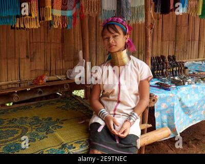 A little girl from the Karen tribe with a unique necklace around her long neck, sits leaning back and waiting for buyers of handicraft products Stock Photo