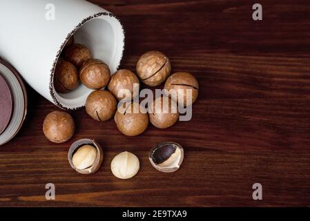 Scattered unshelled macadamia nuts on wooden table. Bowl with macadamia. Selective focus Stock Photo