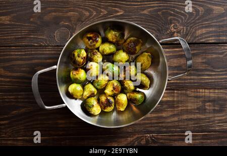 Roasted brussles sprouts in frying pan on wooden background. Top view, flat lay Stock Photo