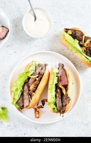Pulled beef sandwiches with caramelized onion on plate over light stone background. Top view, flat lay Stock Photo