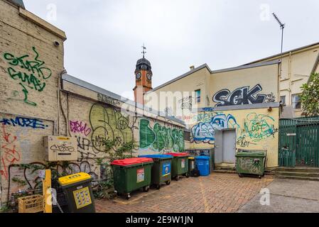 With the heritage listed 1891 Newtown (Sydney) Post Office clock tower in the background the walls of this back lane area are covered in graffiti Stock Photo