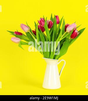 Beautiful spring flowers tulips in vase on yellow background. Festive concept Stock Photo
