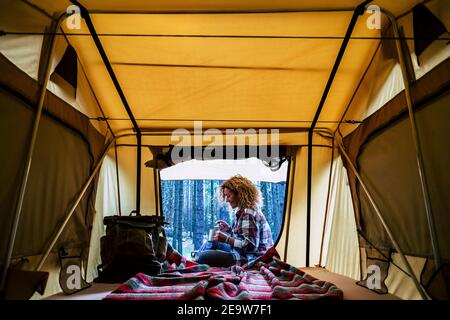 Travel woman sitting in the auto tent and enjoying outdoors from the window with amazing landscape. Best wake up during adventure trip with feeling. C Stock Photo