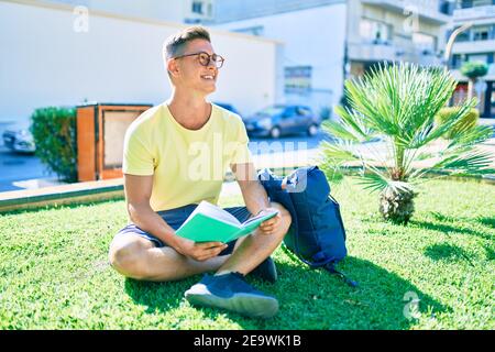 Young hispanic student reading book sitting on the grass at the university campus Stock Photo