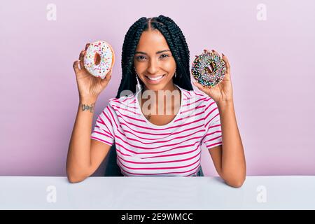 Beautiful hispanic woman holding tasty colorful doughnuts smiling with a happy and cool smile on face. showing teeth. Stock Photo