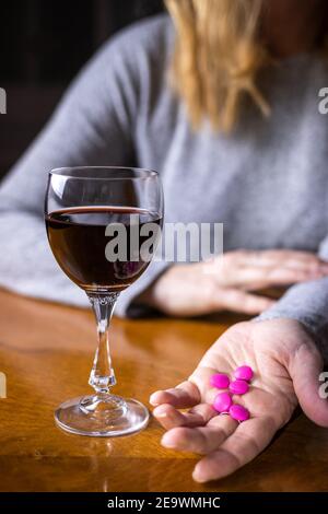Taking pills and drinking alcohol at the same time is bad idea. Drug and alcohol abuse. Red wine in drinking glass on table. Woman holding medicine Stock Photo