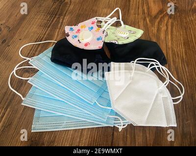 Several different protective masks lie on top of a wooden table, from disposable, to reusable ones Stock Photo