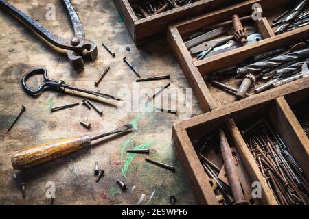 Vintage work tool on wooden table in workshop. Carpentry industrial equipment and toolbox. Messy screwdriver, pliers, hand drill and nail and screws Stock Photo