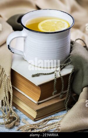 Hot tea drink in mug on books covering by scarf. Still life of teacup on old book. Refreshment during reading Stock Photo