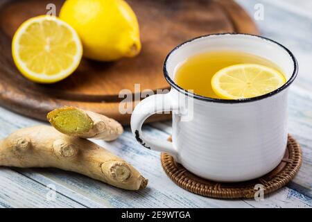 Ginger root and hot tea with slice lemon in white mug. Healthy lifestyle concept. Hot drink in teacup on wooden table Stock Photo