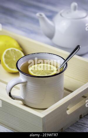 Tea drink with slice lemon in white mug and teapot. Hot drink on serving tray on white wooden table. Refreshment at morning breakfast Stock Photo