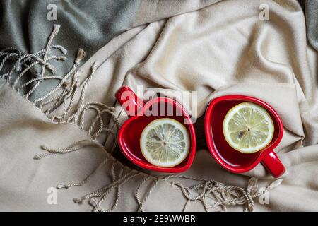 Red heart shape tea cups and scarf, symbol of valentines day. Two hot drinks and plaid at cozy home. Stock Photo