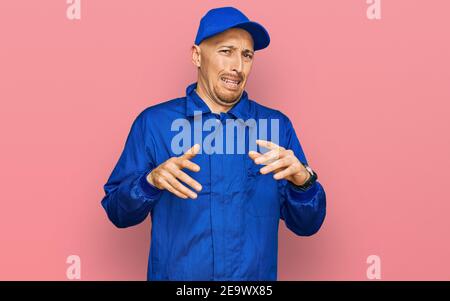 Bald man with beard wearing builder jumpsuit uniform disgusted expression, displeased and fearful doing disgust face because aversion reaction. Stock Photo
