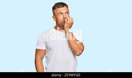 Handsome muscle man wearing casual white tshirt looking stressed and nervous with hands on mouth biting nails. anxiety problem. Stock Photo